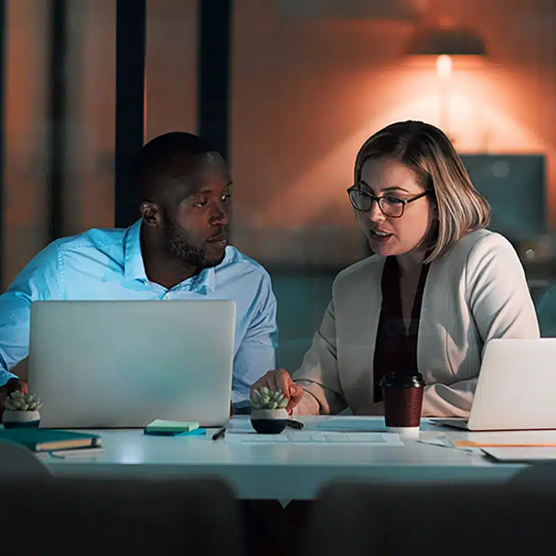 colleagues using a laptop together during a late night in a modern office.