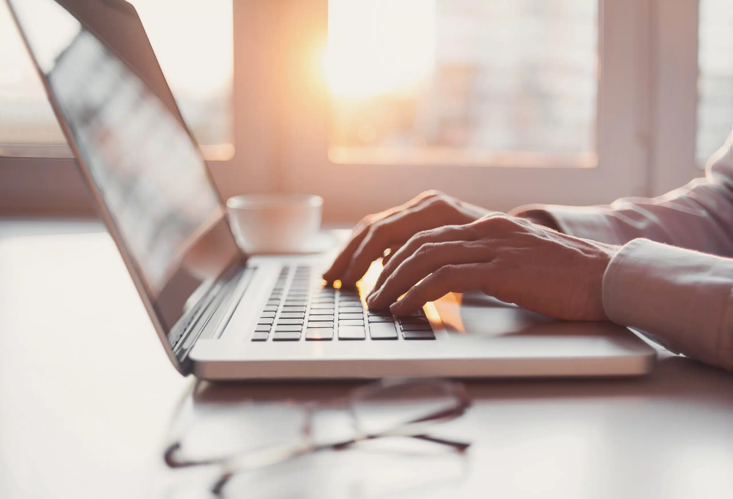 Businessman using smart phone and laptop computer with sun shining through the window behind him.