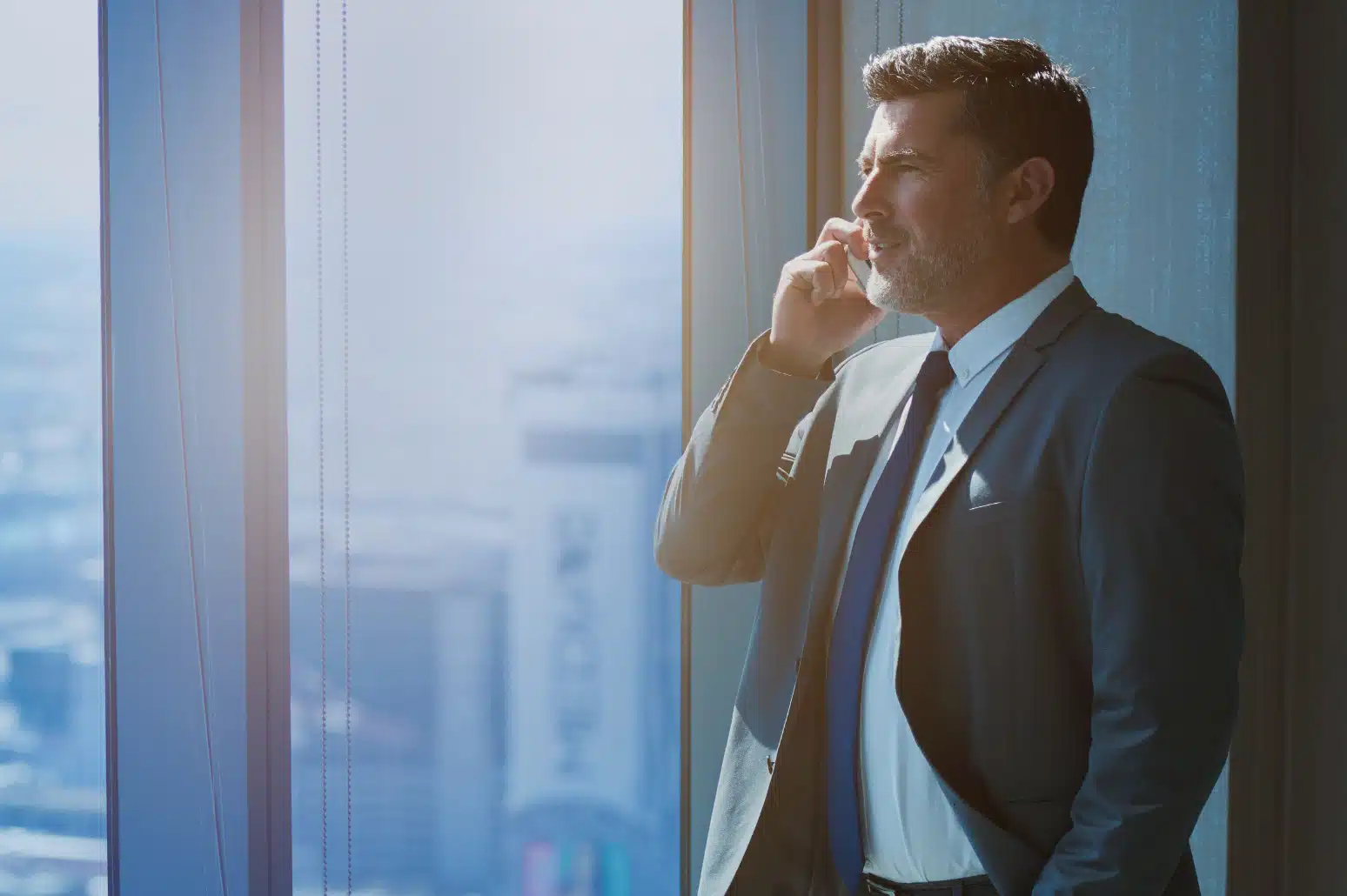 Man stands facing out high rise building window while taking a call.