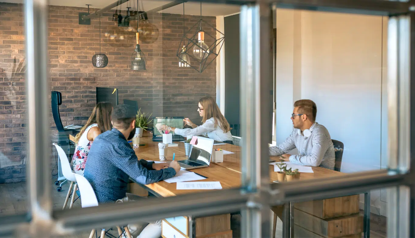 People sit around an office table discussing around an open laptop
