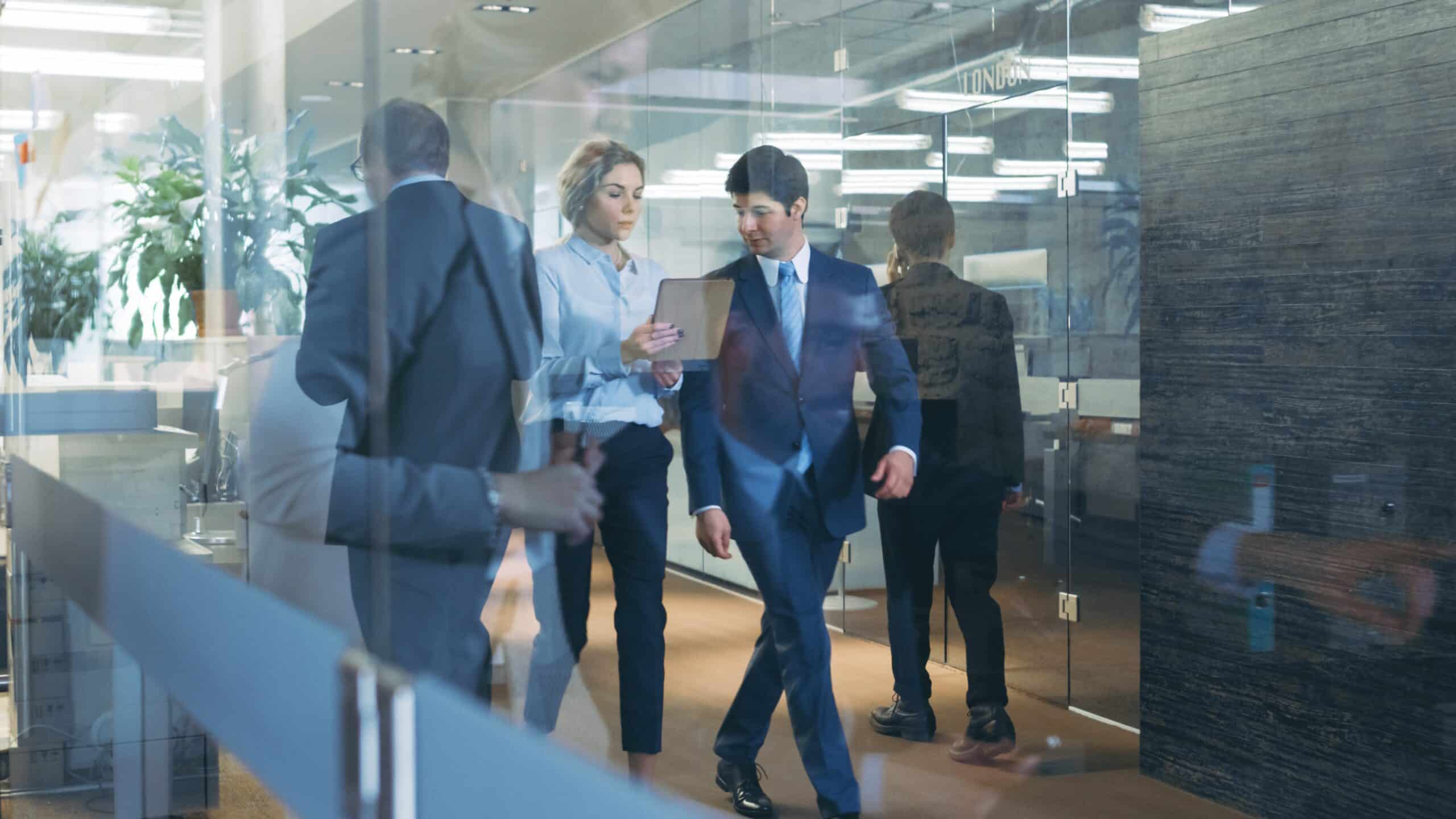 Two business professionals walking down a modern office hallway in conversation.
