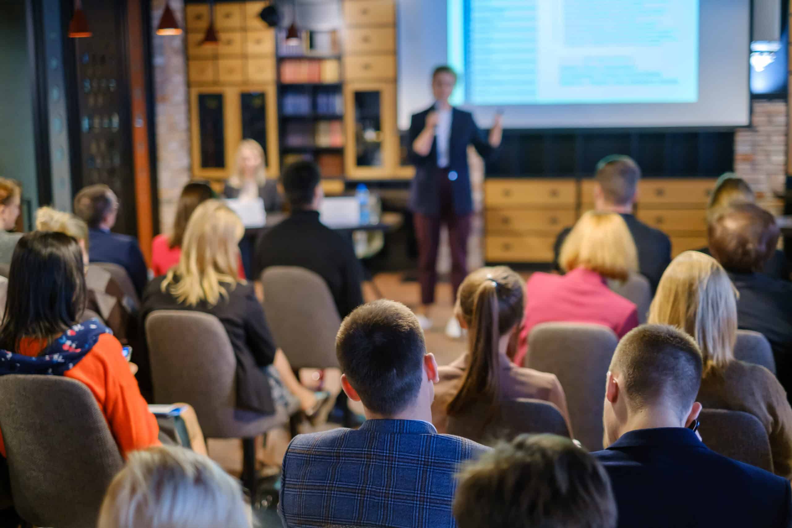 Audience listening to a lecturer at a workshop in a conference hall, representing professional engagement and learning in an executive MBA alumni network.