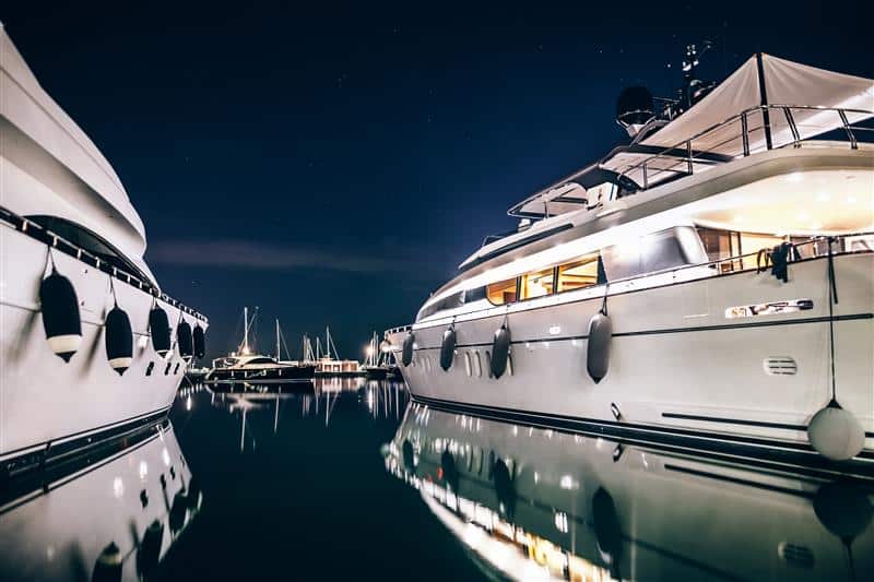 Luxury yachts illuminated at night, showcasing the lifestyle and high-end assets of ultra high net worth (UHNW) individuals, reflecting global UHNW luxury trends and spending patterns in 2024.