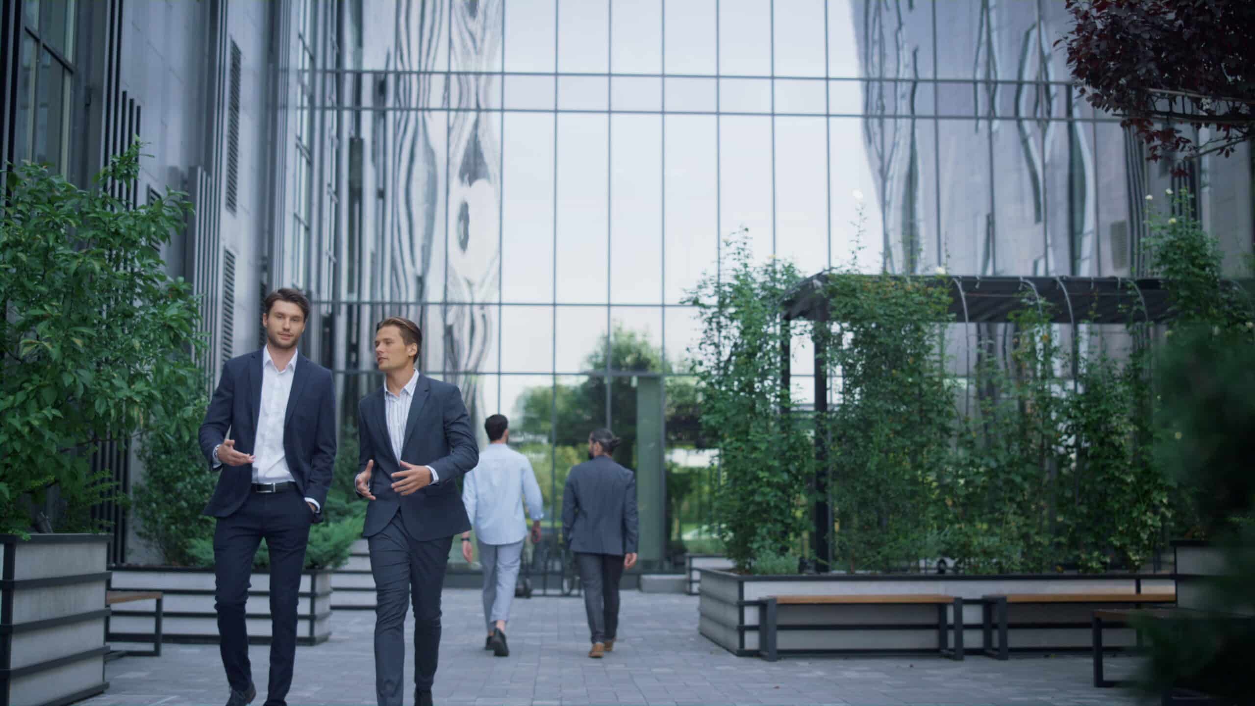 Two business professionals in suits walking outside an office building, talking and building a professional relationship