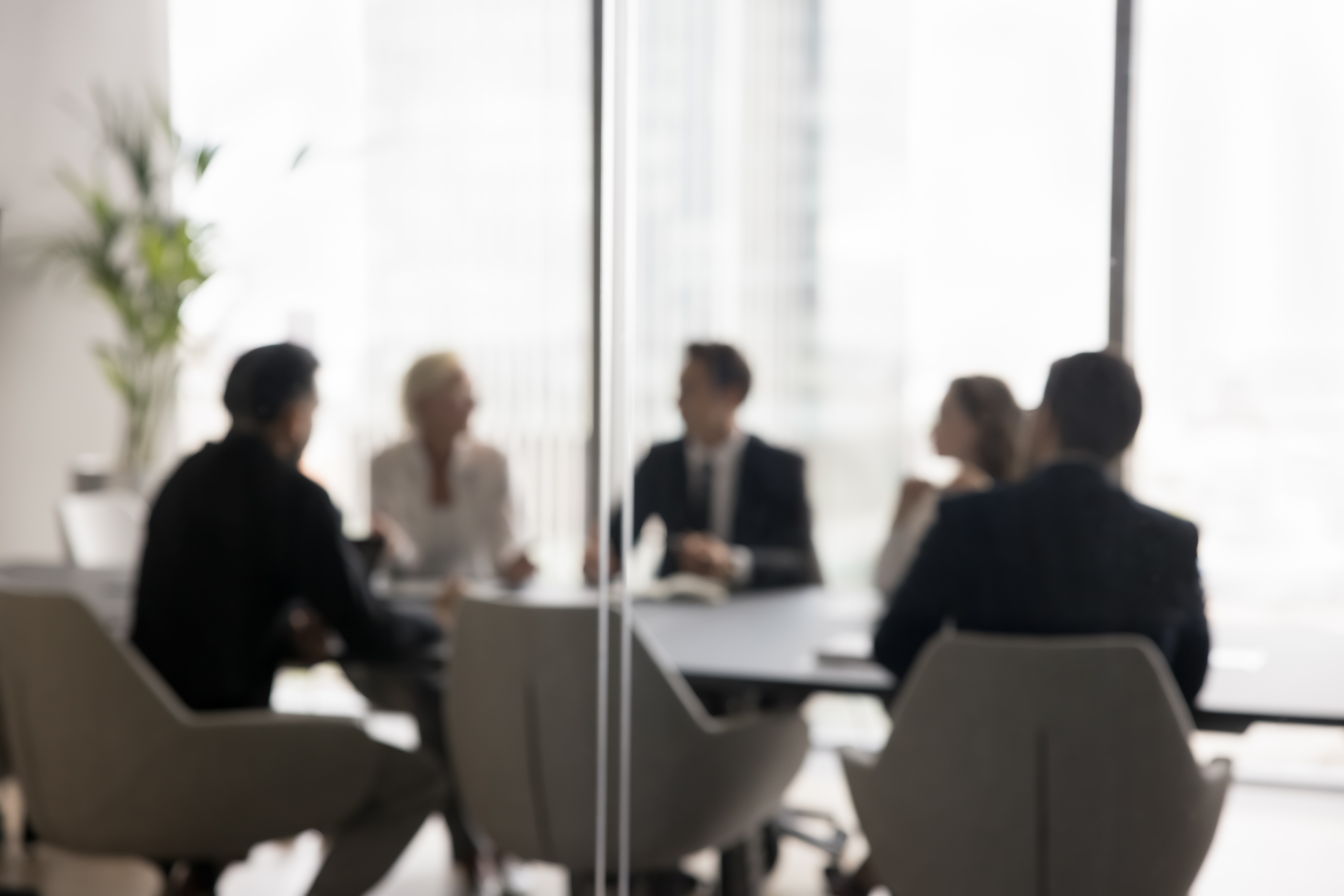 Blurred image of business leaders seated around a boardroom table in discussion.