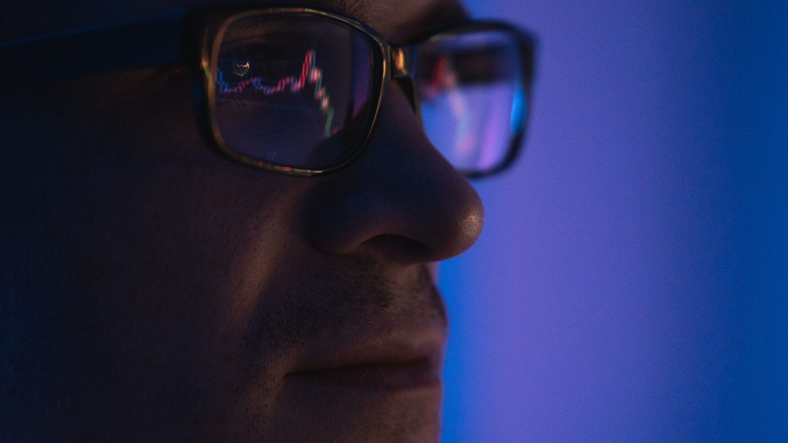 Close-up of a man in glasses in a dimly lit room, with stock market data reflected in the lenses, illustrating investor focus amid major market events like the SpaceX IPO.