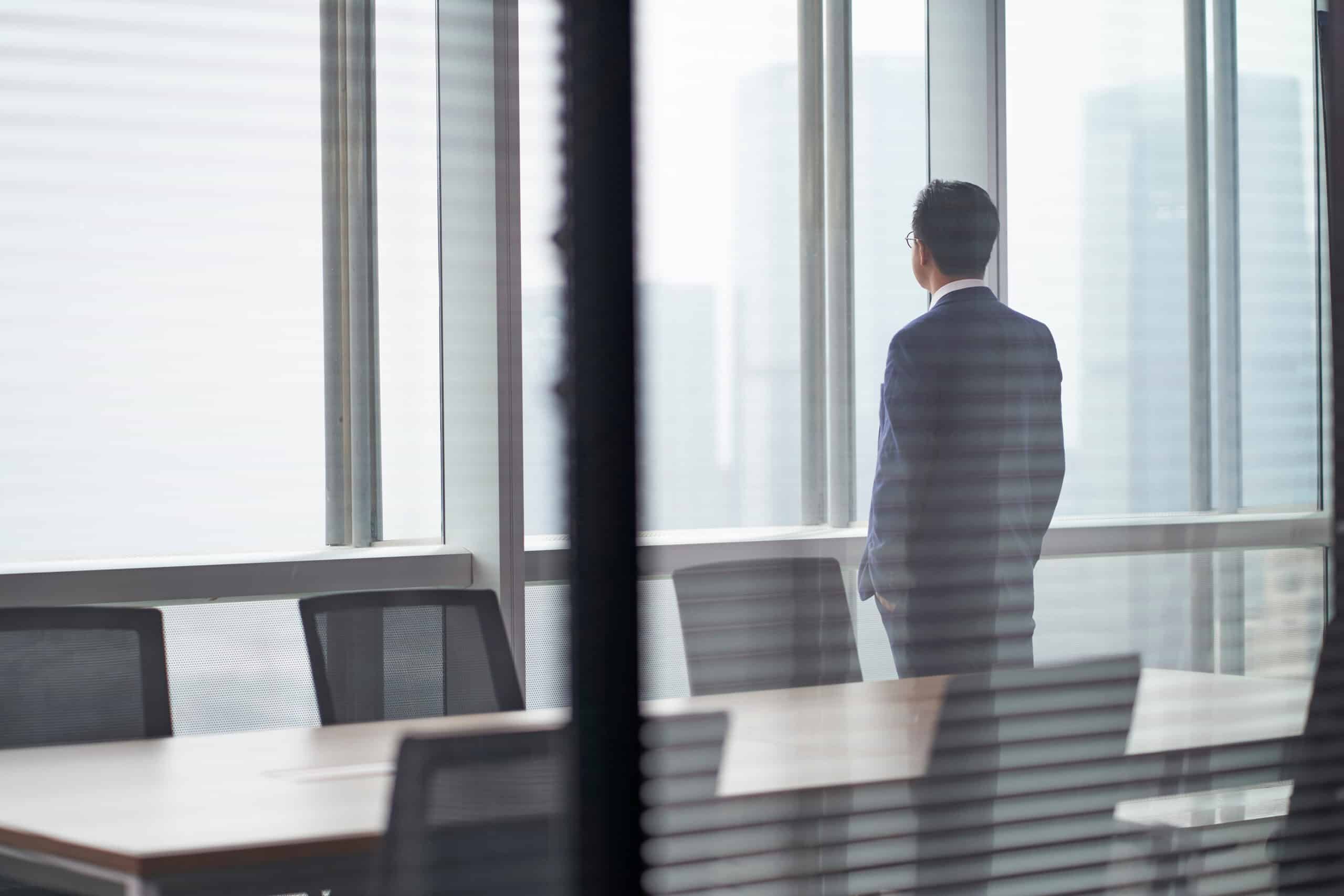 Executive in a suit looking out an office window, representing new leadership and executive intelligence