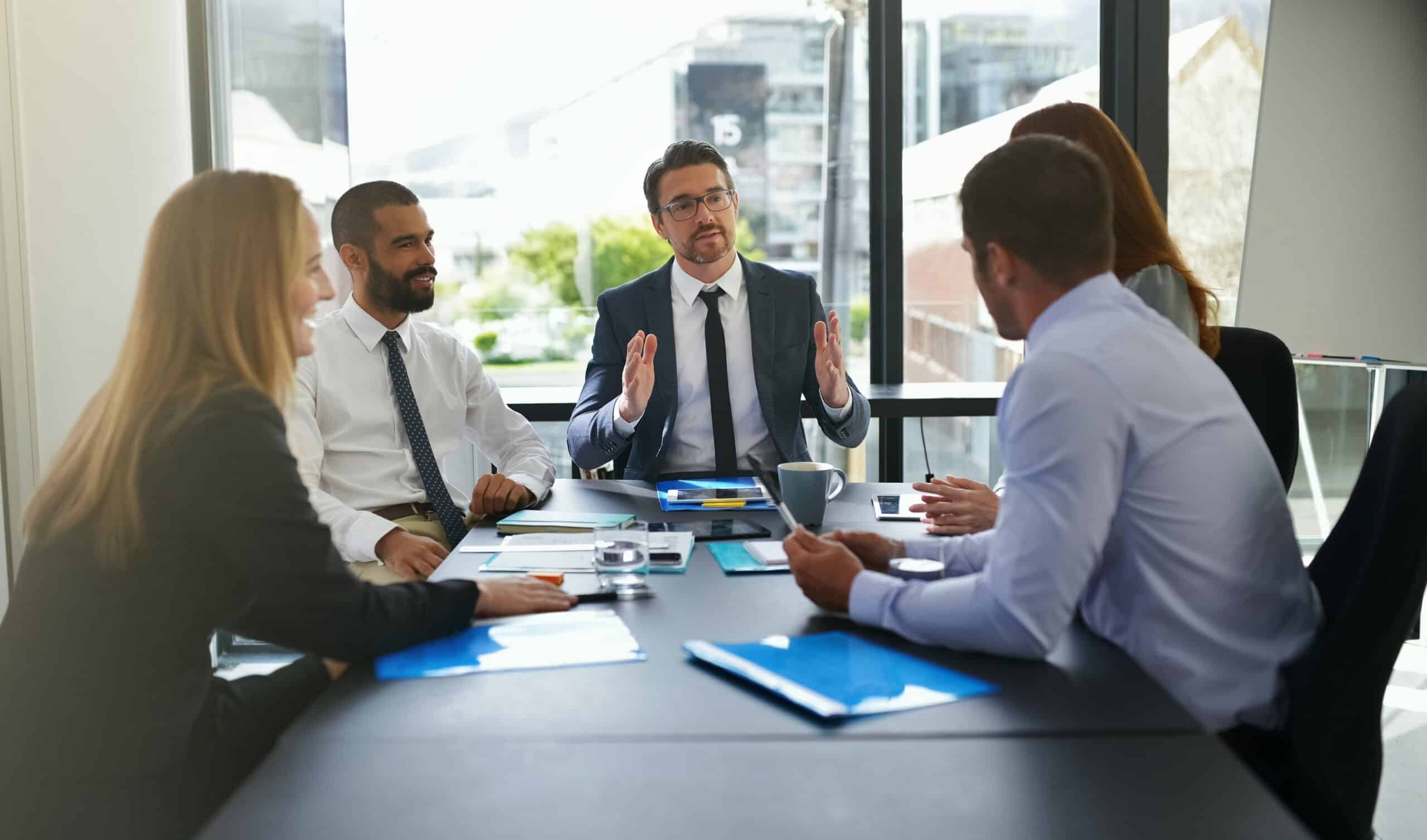 Investment banking professionals discussing firmwide relationships and deal flow during a team meeting.