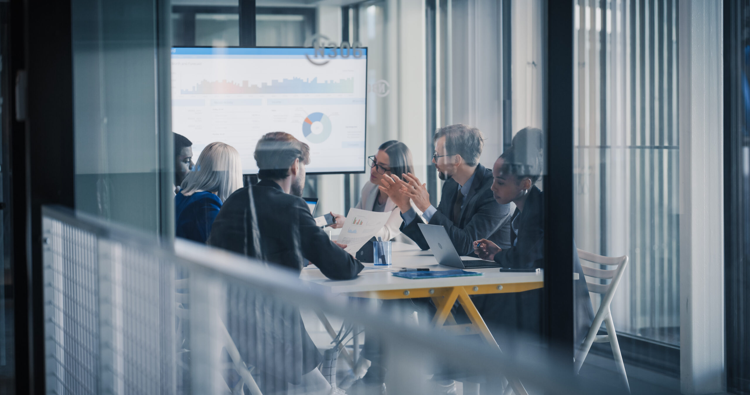 Business team meeting in a glass conference room reviewing data on a screen, illustrating DSG Global's board research process using Altrata's BoardEx