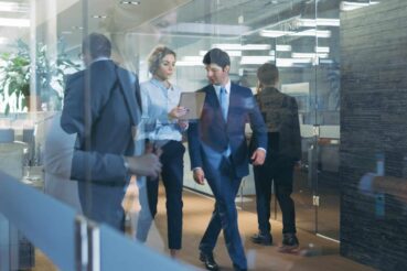 Two business professionals walking down a modern office hallway in conversation.